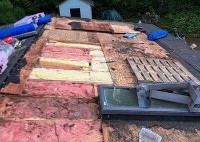 Roof under renovation with insulation panels and debris scattered, showing exposed structure.