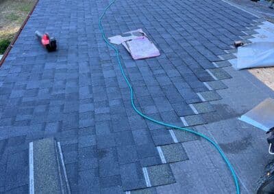 Roofing installation with black shingles, tools, and equipment on a sloped surface.