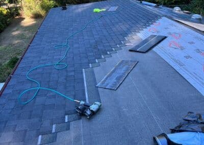Roofing installation process with shingles, tools, and hose on a sloped roof.