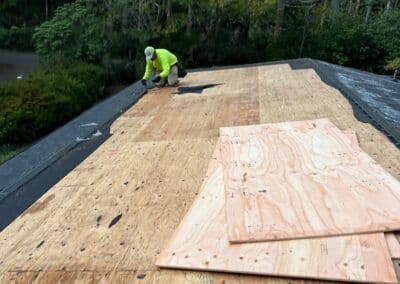 Worker installing plywood on a roof for construction, surrounded by greenery.