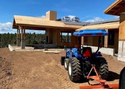 Construction site with tractor and partially built wooden house against clear blue sky.