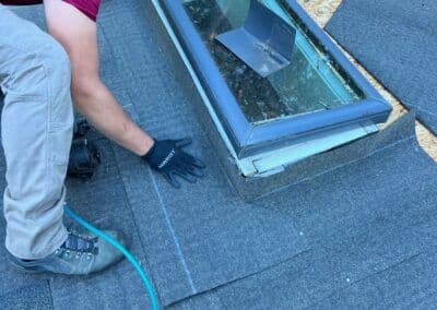 Roofer installing roofing material around a skylight on a residential roof.