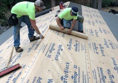 Two workers installing WaterBlock roofing underlayment on a sloped roof. Safety gear visible.