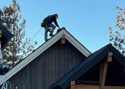 Roofer installing shingles on a residential roof with trees in the background.