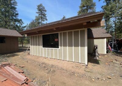 Newly constructed cabin exterior with green siding and large window in wooded area.