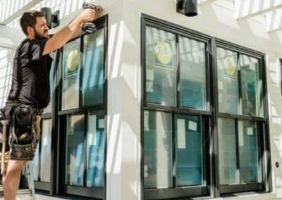 Carpenter installing new windows with a power drill on a modern home exterior.