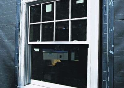 Newly installed double-hung window with grid design, surrounded by black house wrap.