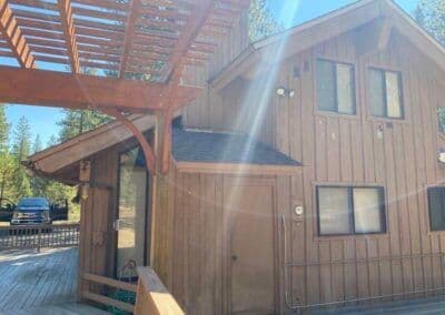 Wooden cabin exterior with sunlit balcony and surrounded by trees in a forest setting.