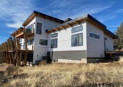 Modern mountain home with large deck and multiple windows, set against a scenic backdrop.