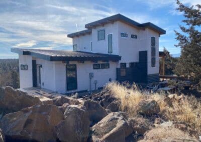 Modern mountain home surrounded by rocky terrain and natural landscape under a blue sky.