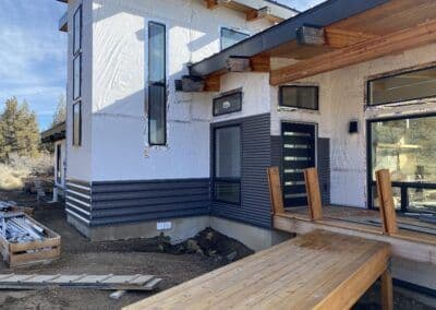 Modern home exterior with wood accents, large windows, and construction materials on site.