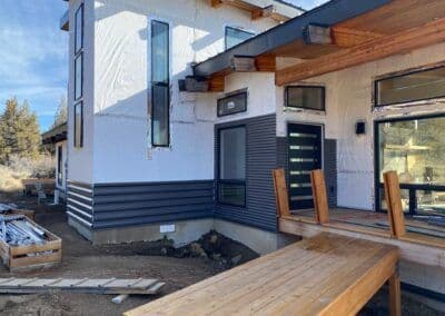 Modern home exterior with wood accents, large windows, and a wooden deck under construction.