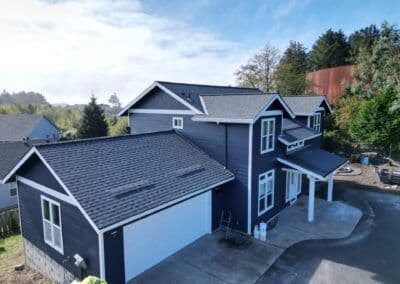 Modern dark blue house with white trim and garage, surrounded by trees and open space.
