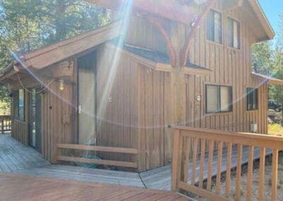 Wooden cabin with a deck in a forested area, sunlight streaming through the trees.