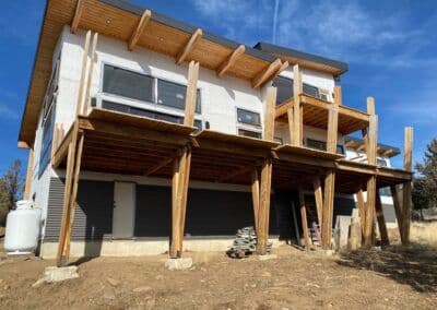 Modern home under construction with wooden deck and supports, surrounded by outdoor space.