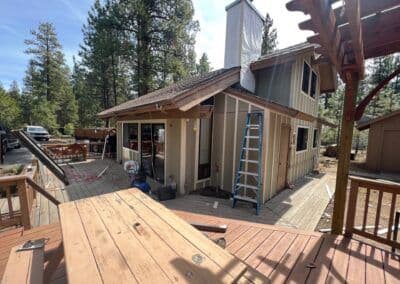 House renovation featuring a wooden deck, ladder, and colorful trees in the background.