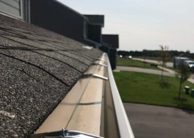 Close-up of a residential roof gutter system against a clear sky and landscaped area.