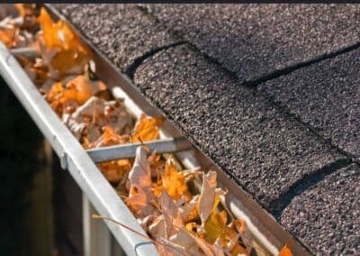 Clogged gutters filled with fallen leaves on a roof, highlighting autumn maintenance needs.