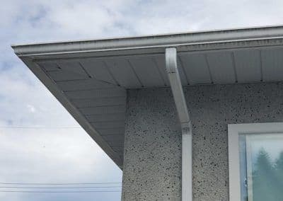 Corner of a modern house showing exterior detail and overhang against a cloudy sky.