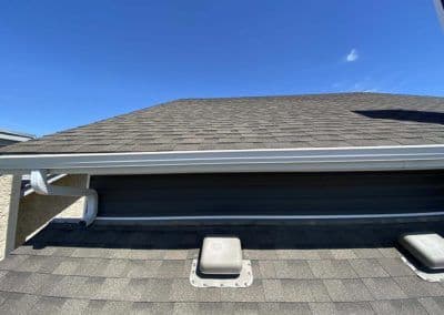 Close-up of a residential roof with asphalt shingles and ventilation pipes under clear blue sky.