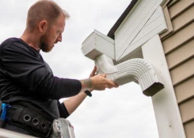Man installing a white gutter attachment on a house's exterior.