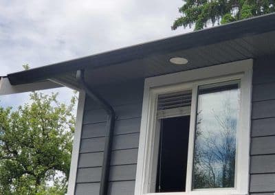 Modern house exterior with gray siding, overhang, and window against a cloudy sky.