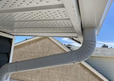 Metal gutter downspout attached to a house roof with clear blue sky in the background.
